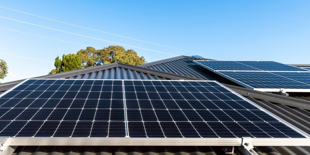 Pigeon/Possum Protection 4 Solar panels fitted on the roof of a house in Brisbane, with trees and a clear blue sky in the background. Power lines are visible above the roof.