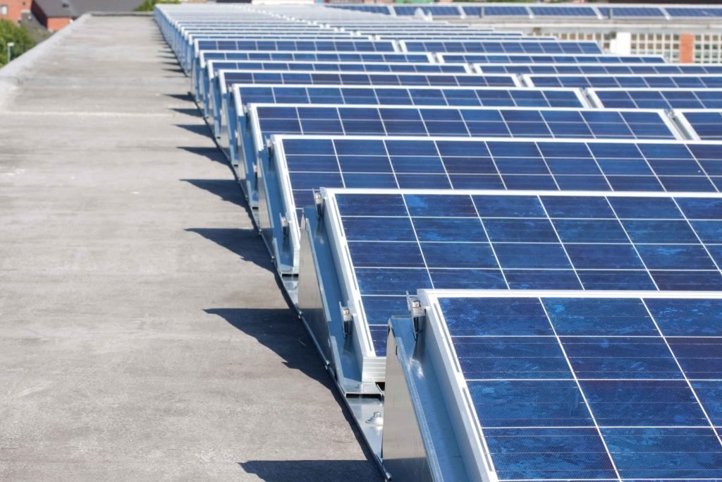Commercial Solar Health Checks 3 Rows of blue solar panels are installed on a flat rooftop in Brisbane, extending into the distance under clear skies. The panels are angled to capture solar energy efficiently, making the most of the abundant Sunshine Coast sunlight.