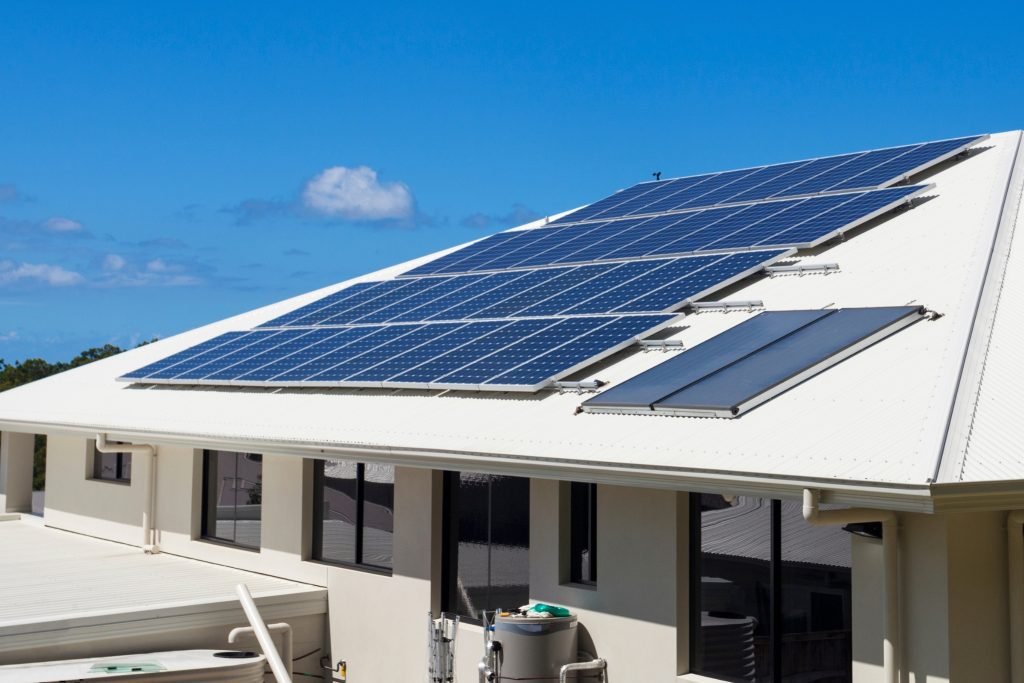 A white house with solar panels installed on its sloping roof under a clear blue sky in Brisbane. The solar panels are arranged in groups, efficiently capturing sunlight for renewable energy.