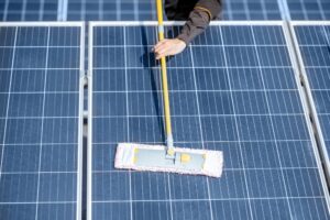 Solar Maintenance 101: A Homeowner's Guide 1 Person cleaning solar panels with a long-handled mop on a sunny day