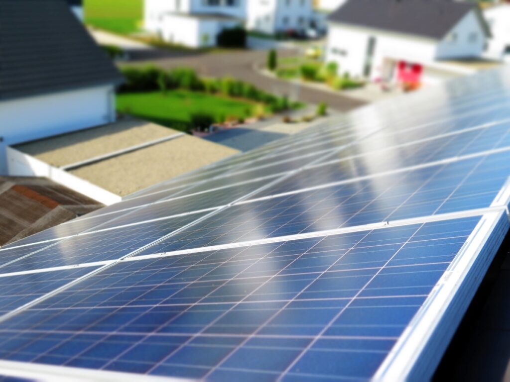 Close-up of solar panels on a rooftop, with residential houses and greenery blurred in the background, illustrating the use of solar energy in a suburban Sunshine Coast neighbourhood.