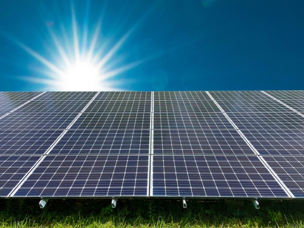 Rows of solar panels on grass reflect sunlight under a clear blue sky, capturing solar energy as the sun shines brightly—an ideal scene for Brisbane or Sunshine Coast sustainability.