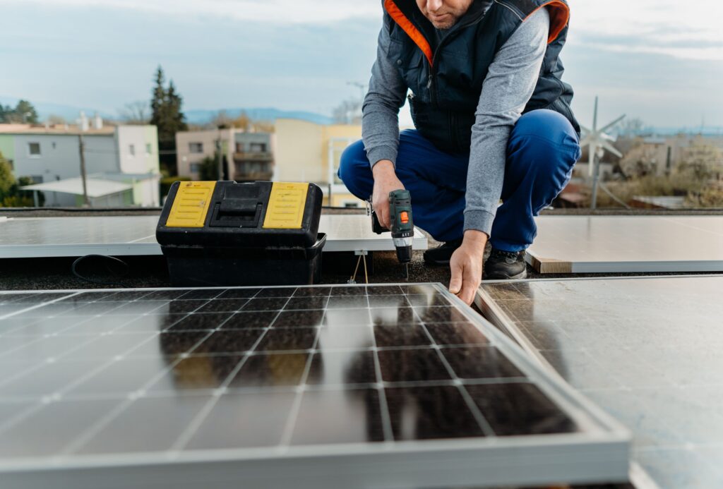 Crouched technician drilling during solar panel installation on a rooftop, emphasizing professional solar installation services and attention to detail.
