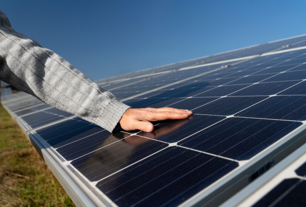Hand inspecting the surface of a solar panel under a clear blue sky, demonstrating quality checks and maintenance to ensure optimal performance.